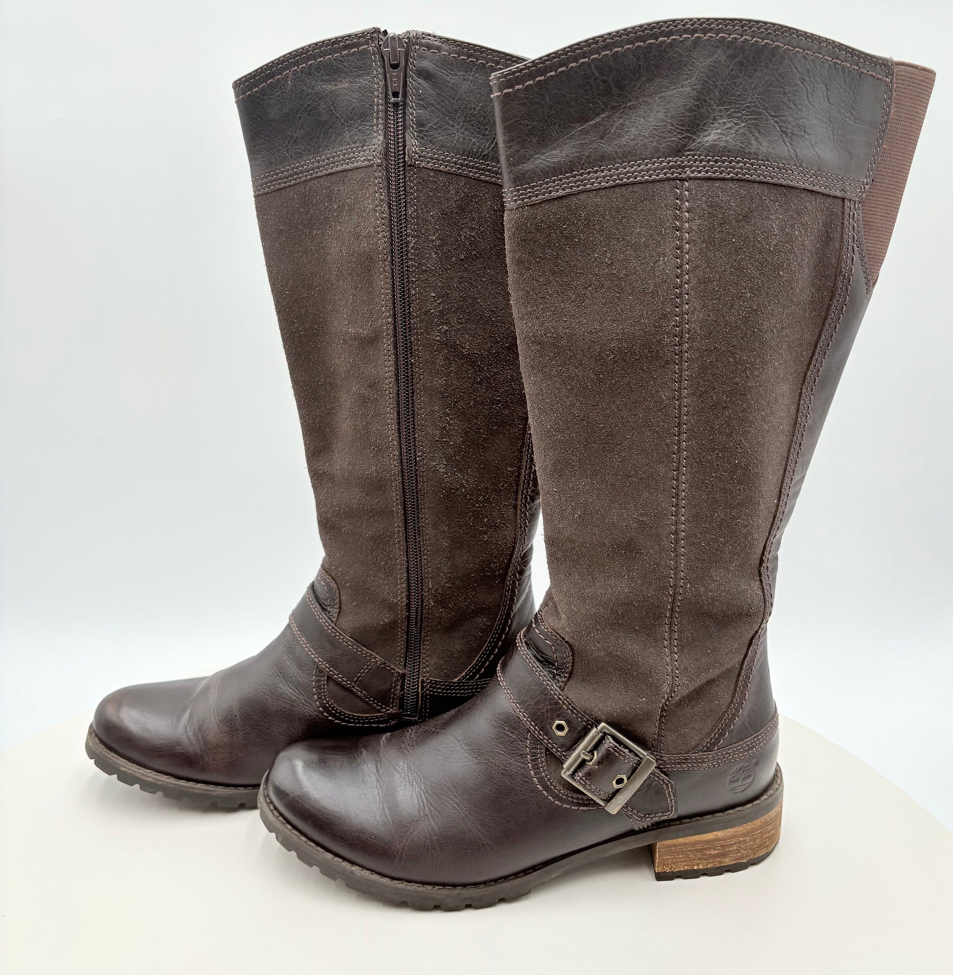 Pair of brown knee-high boots with a buckle on a white background