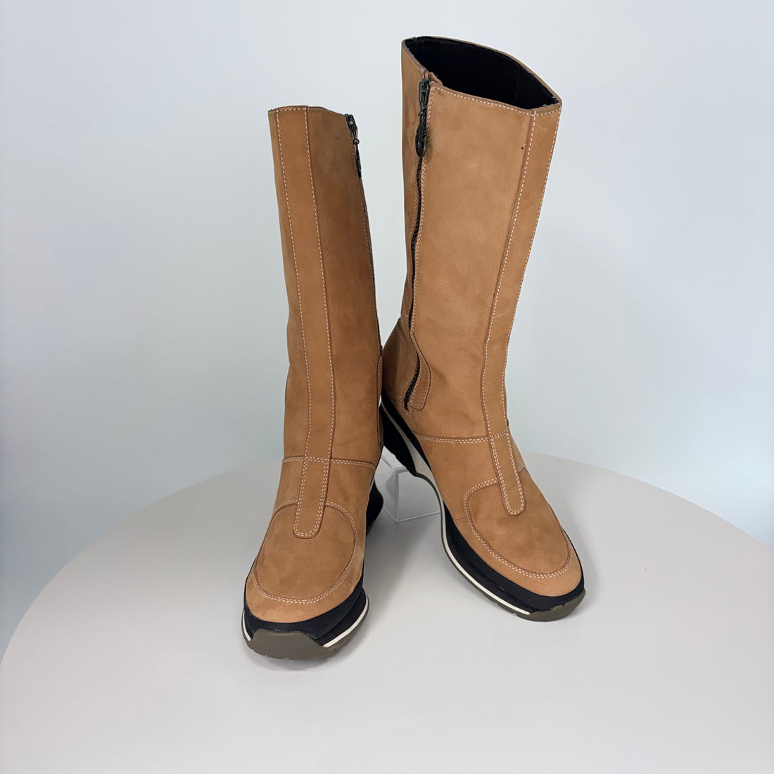 Pair of tan knee-high boots with black soles on a white background