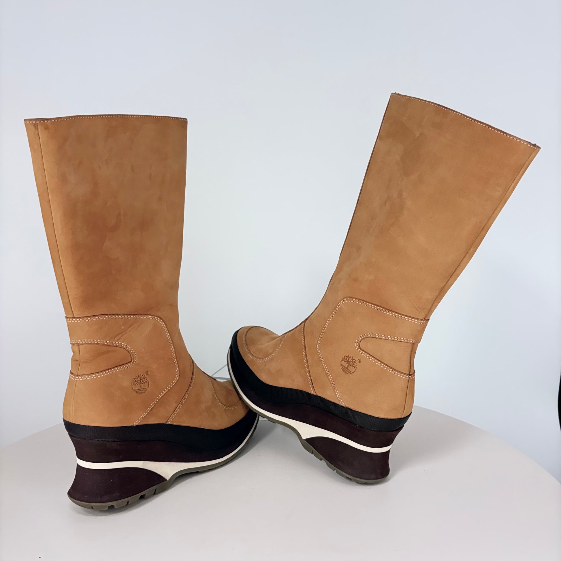 Pair of tan knee-high boots with black soles on a white background