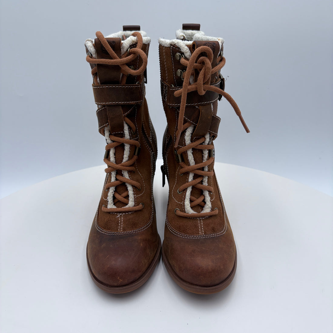 Pair of brown lace-up boots with white lining on a light gray background