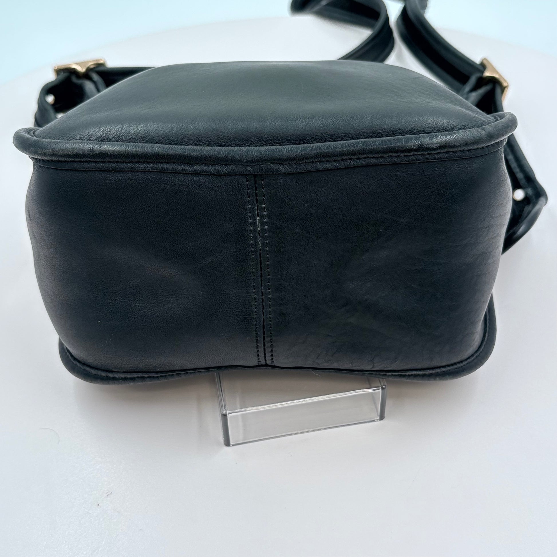 Black leather bag on a clear stand against a white background
