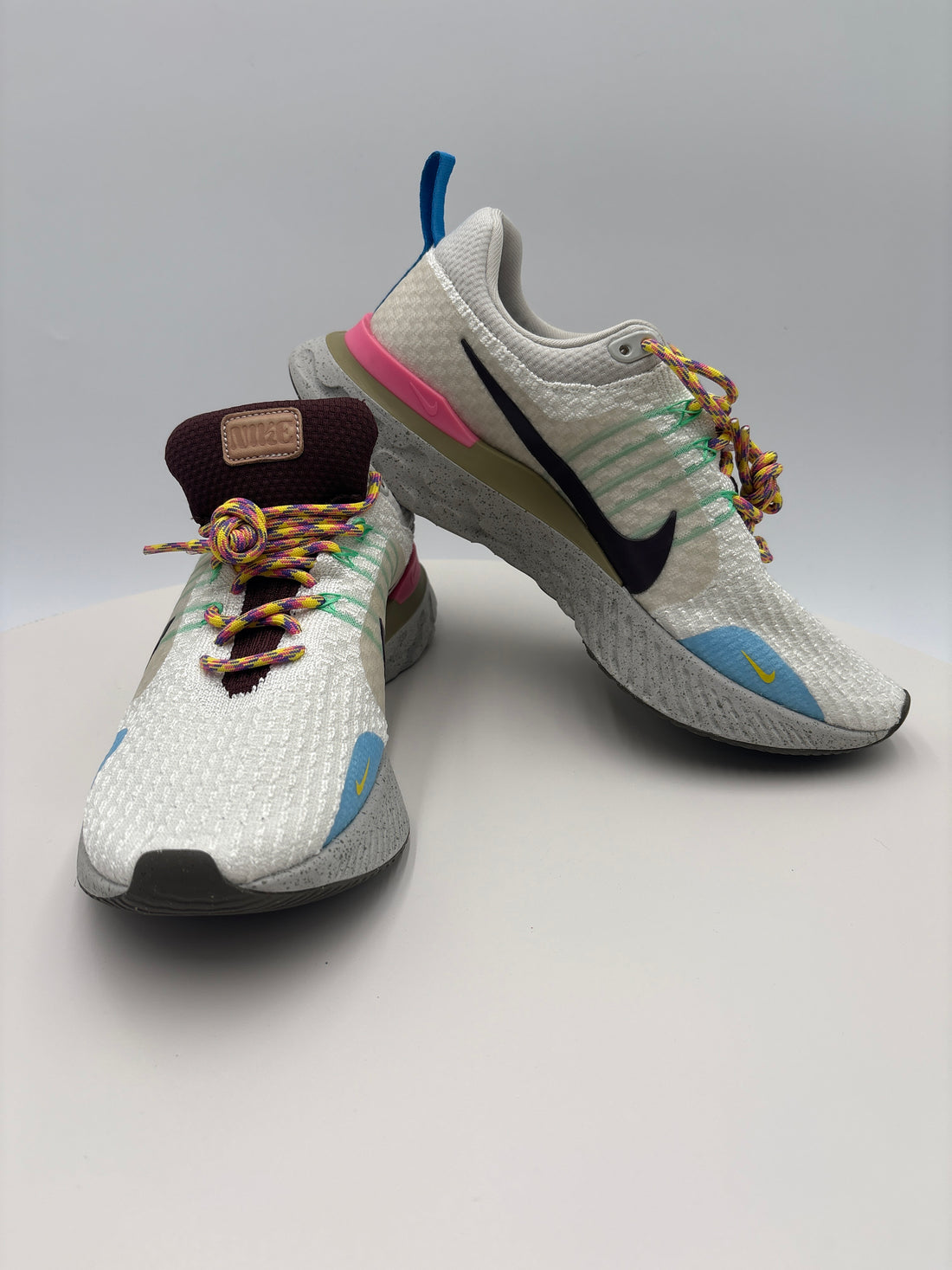 Pair of white sneakers with colorful laces on a white surface, accompanied by a certificate of authenticity.